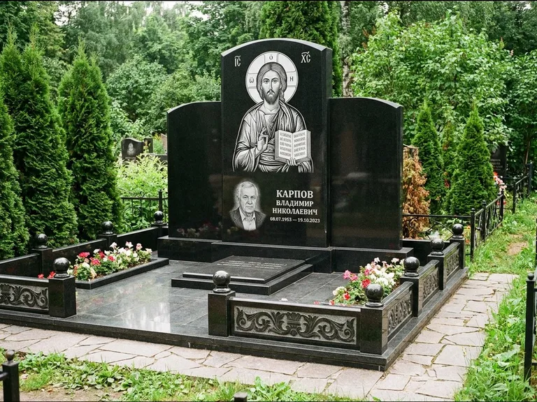 Памятник с гравировкой иконы: широкая панорамная стела с золочёным нимбом — гравировка образа Матроны Московской, цветник с белыми хризантемами, работа «Мельникова» в Краснодаре