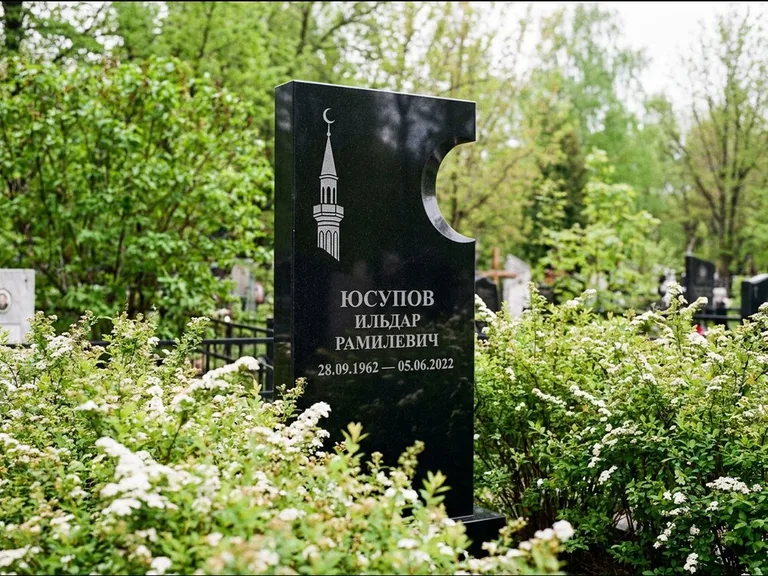 Мусульманский памятник с гравировкой мечети: стела с боковым вырезом в форме полумесяца — гравировка минарета с полумесяцем, низкие кусты спиреи в цвету, работа «Юсупов» в Краснодаре